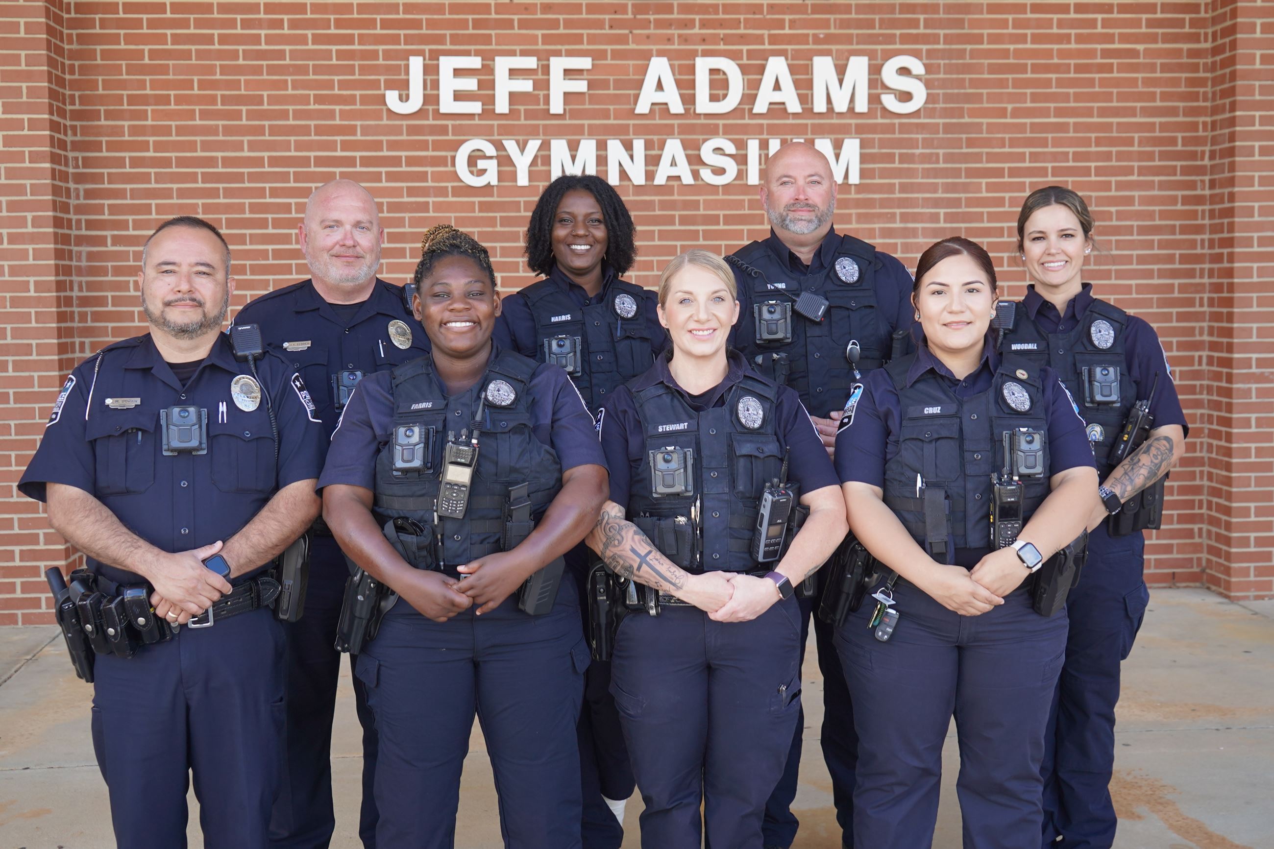 Clayton Student Resource Officerspose for a group photo in front of Jeff Adams Gymnasium
